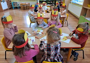 Przedszkolaki przy stolikach kolorują sylwety Kubusia Puchatka.